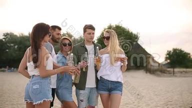 一群朋友在日落时分在海滩上玩着享受饮料和放松的乐趣。 男女青年